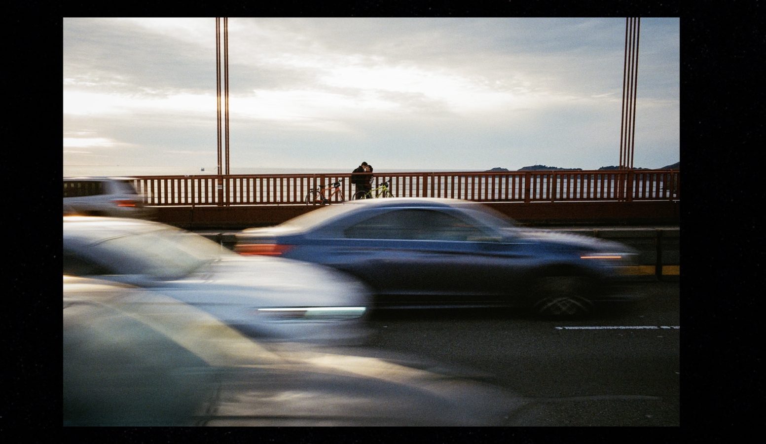 a couple on the Golden Gate Bridge with cars passing