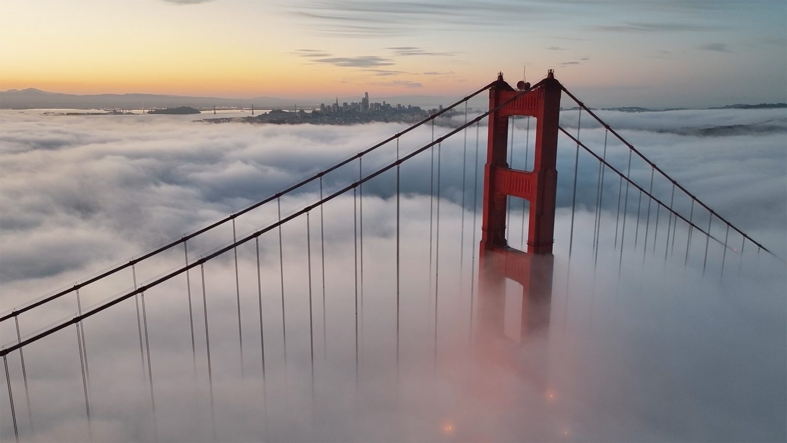 Golden Gate Bridge towers above fog at sunrise