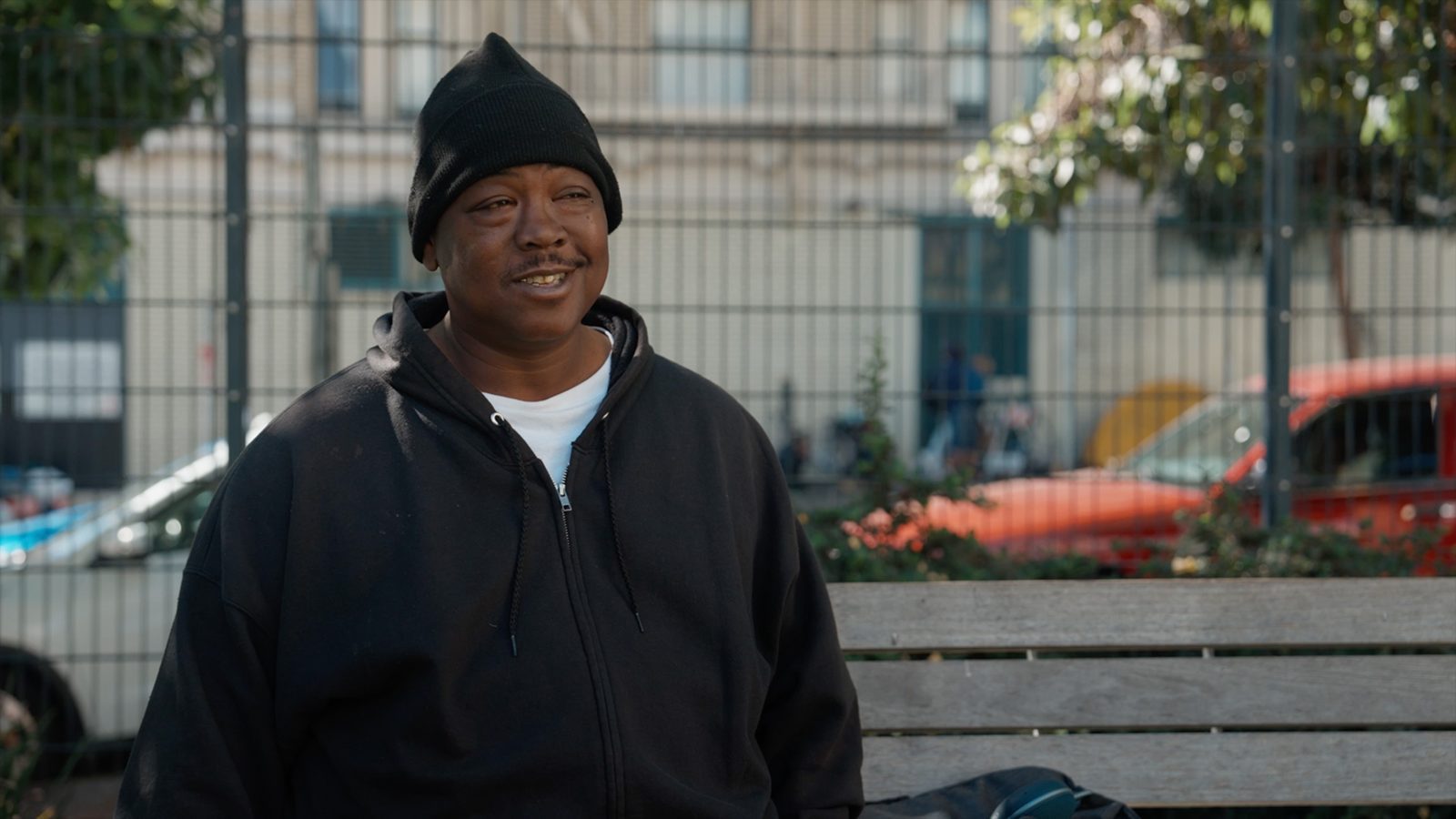 a smiling man in a black beanie by a fence